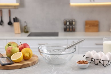 Metal whisk, bowl, grater and different products on gray marble table in kitchen