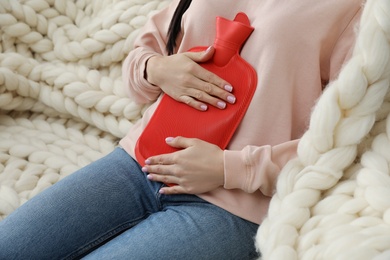 Photo of Woman using hot water bottle to relieve menstrual pain at home, closeup