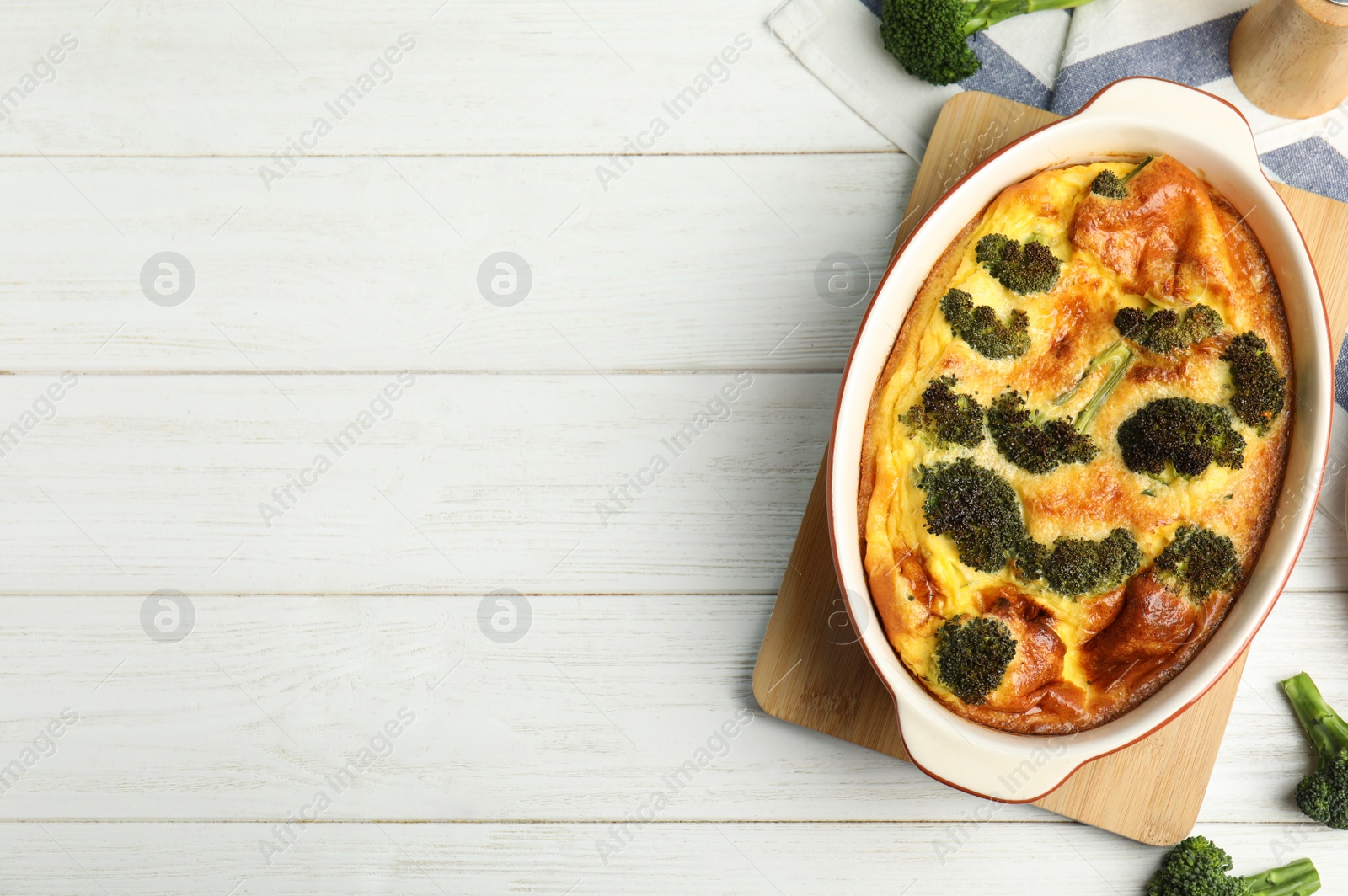 Photo of Tasty broccoli casserole in baking dish on white wooden table, flat lay. Space for text