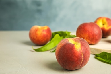 Tasty fresh peaches with leaves on grey table against blue background, space for text