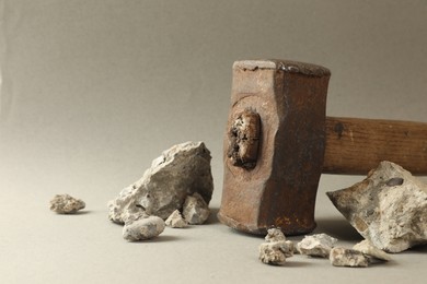 Photo of One sledgehammer and pieces of broken stones on grey background, closeup. Space for text