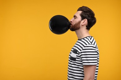 Photo of Man inflating black balloon on yellow background. Space for text