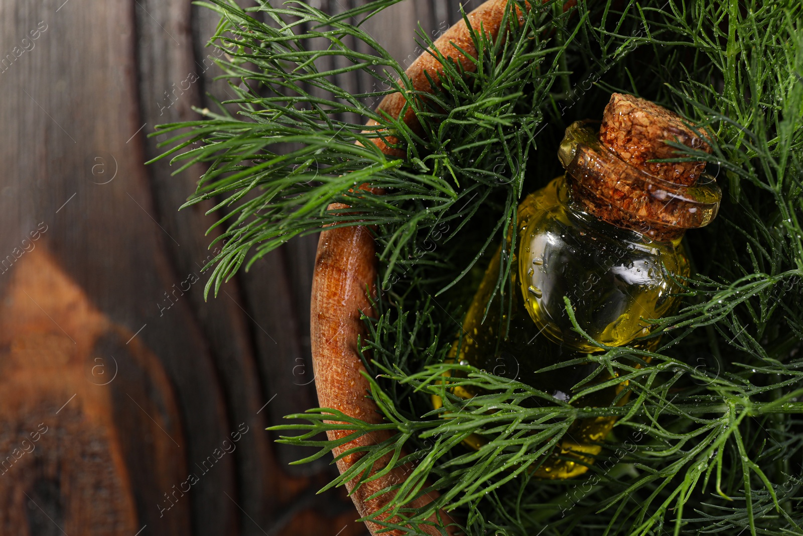 Photo of Bowl with bottle of essential oil and fresh dill on dark wooden table, top view. Space for text