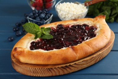 Photo of Delicious sweet cottage cheese pastry with cherry jam on blue wooden table, closeup