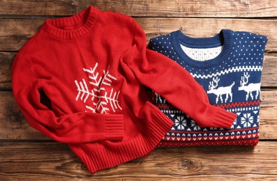 Christmas sweaters with pattern on wooden background, top view