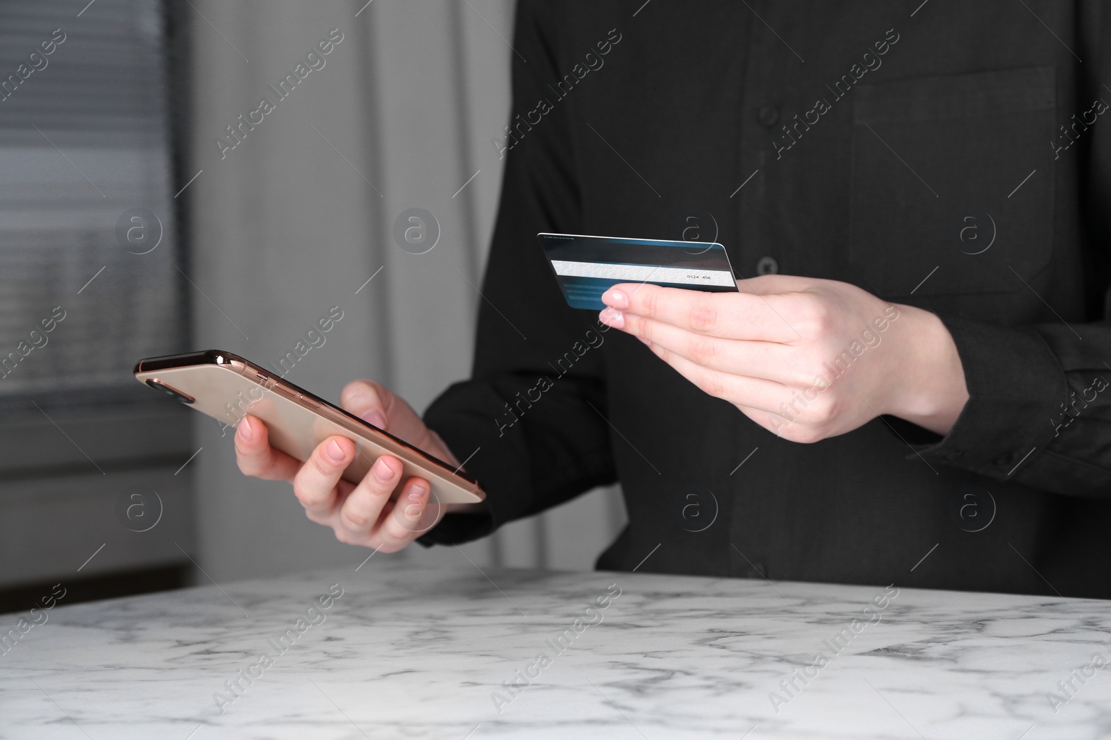 Photo of Online payment. Woman with smartphone and credit card at white marble table indoors, closeup