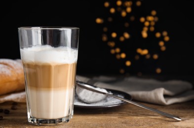 Photo of Delicious latte macchiato, croissant and coffee beans on wooden table. Space for text