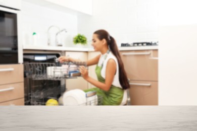 Image of Young woman loading dishwasher in kitchen, focus on empty table