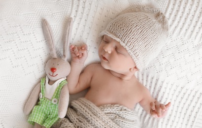 Adorable newborn baby with toy bunny lying on bed