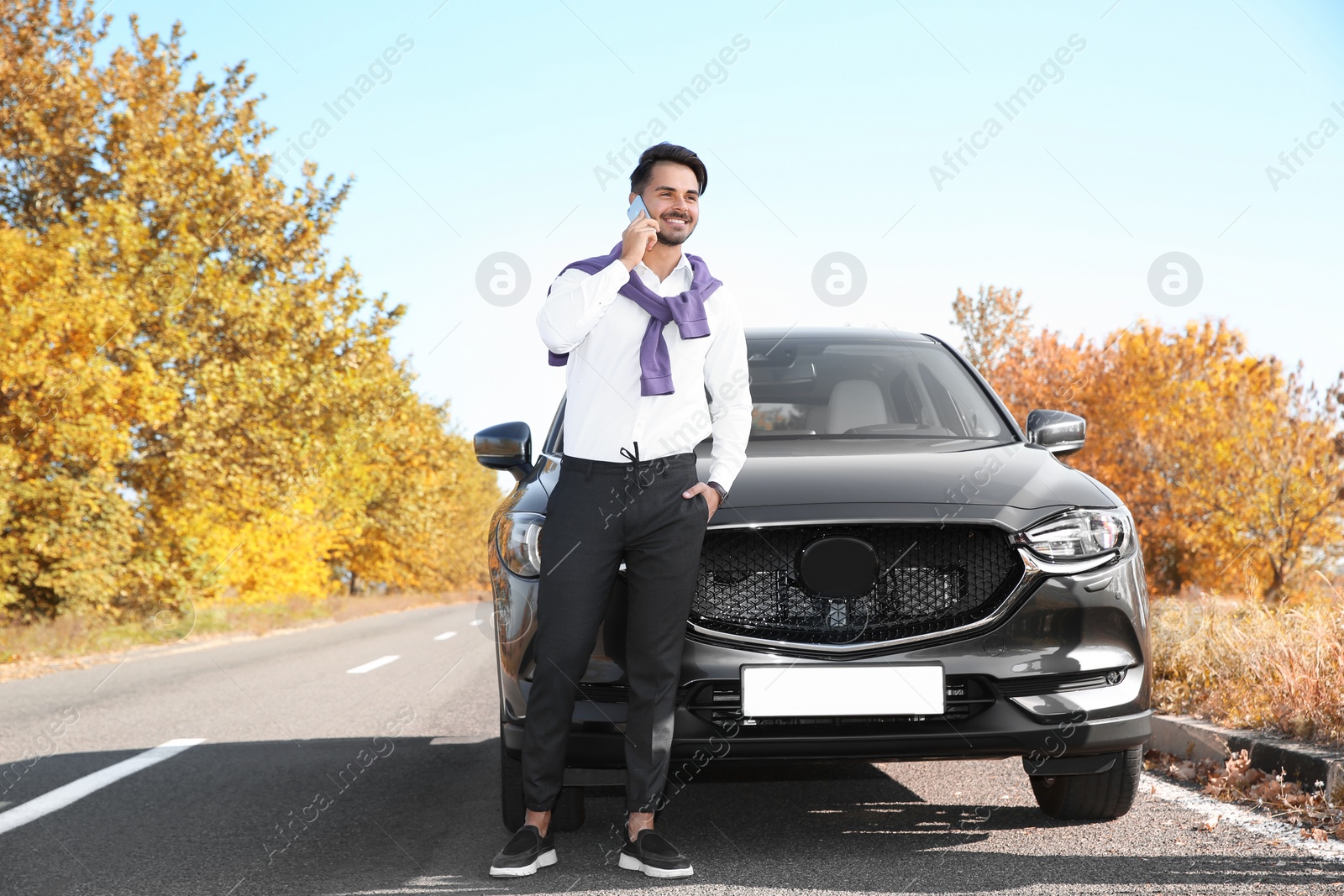 Photo of Young man talking on phone near modern car, outdoors