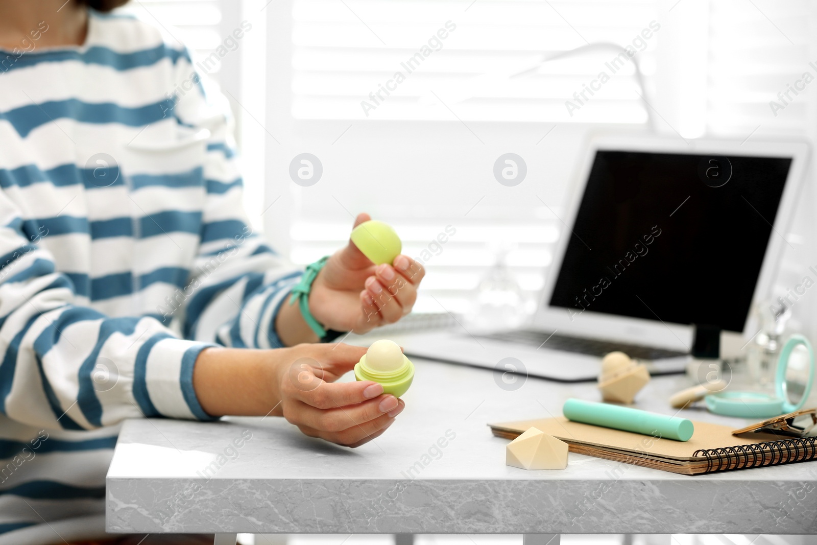 Photo of Young beauty blogger with lip balm at light grey marble table, closeup