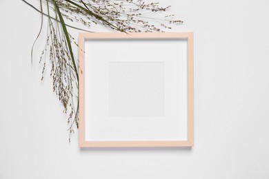 Photo of Empty photo frame and wild flowers on white background, top view. Space for design