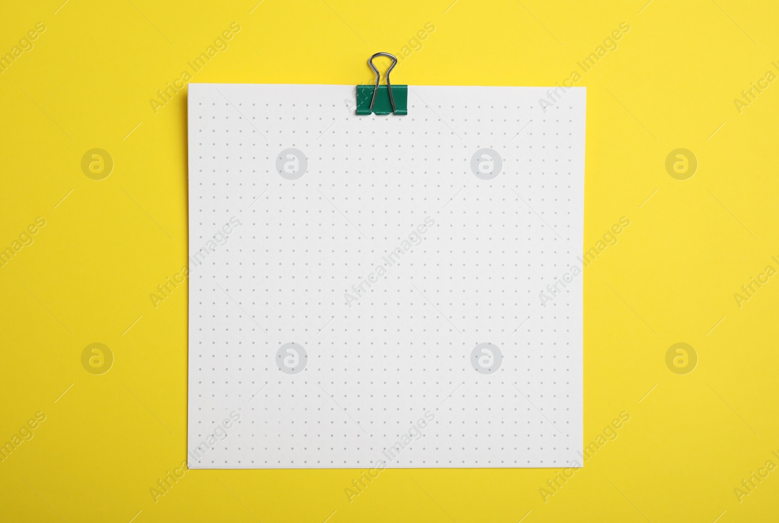 Photo of Sheet of paper with clip on yellow background, top view