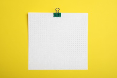 Sheet of paper with clip on yellow background, top view