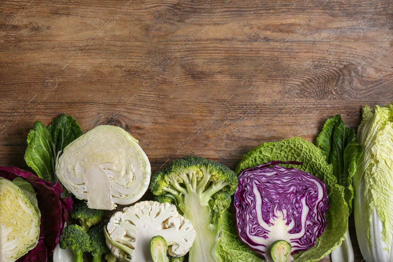 Photo of Different whole and cut types of cabbage on wooden table, flat lay. Space for text