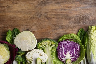 Different whole and cut types of cabbage on wooden table, flat lay. Space for text