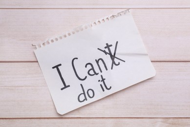 Photo of Motivation concept. Changing phrase from I Can't Do It into I Can Do It by crossing out letter T on light wooden table, top view