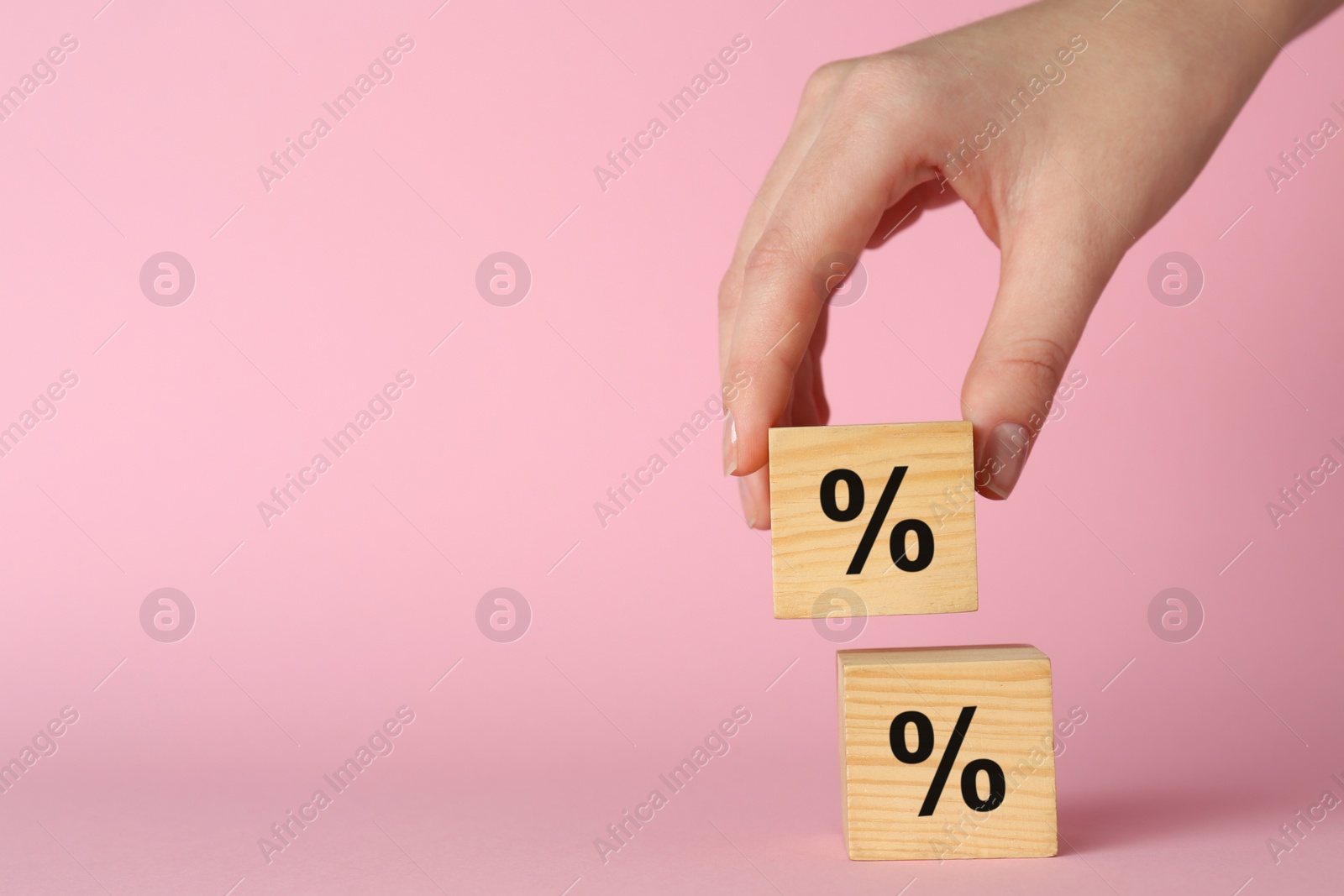 Photo of Woman stacking wooden cubes with percent signs on light pink background, closeup. Space for text