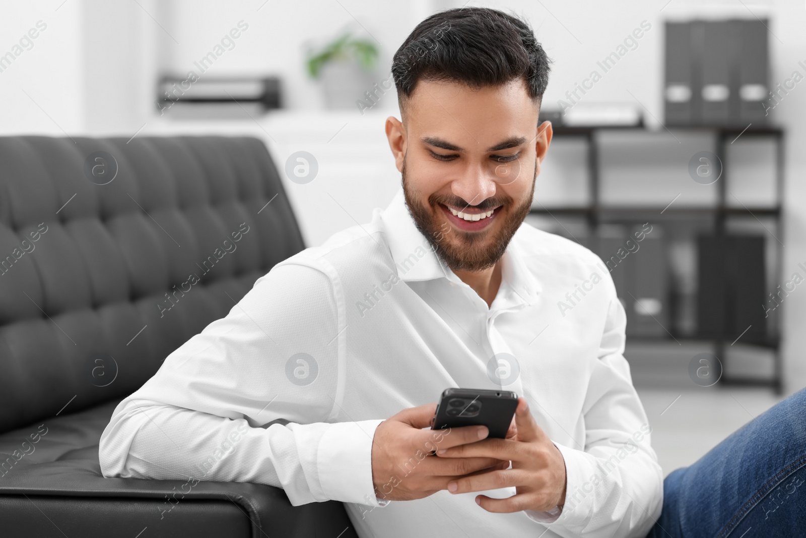 Photo of Handsome young man using smartphone in office