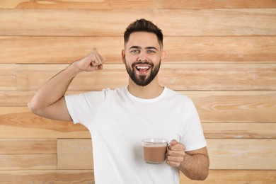Photo of Young man with glass cupchocolate milk showing his strength on wooden background