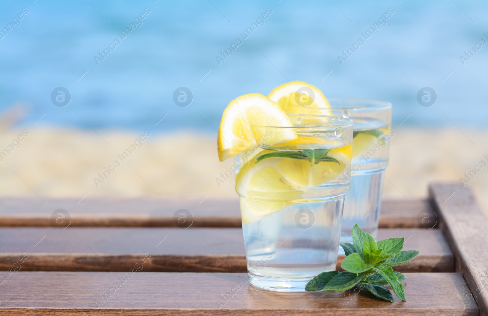 Photo of Refreshing water with lemon and mint on wooden table outdoors, space for text