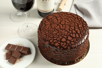 Photo of Delicious truffle cake, chocolate pieces and red wine on light wooden table