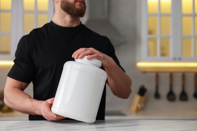 Young man with jar of protein powder at white marble table in kitchen, closeup