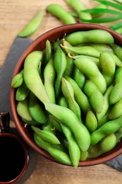 Green edamame beans in pods served with soy sauce on wooden table, flat lay