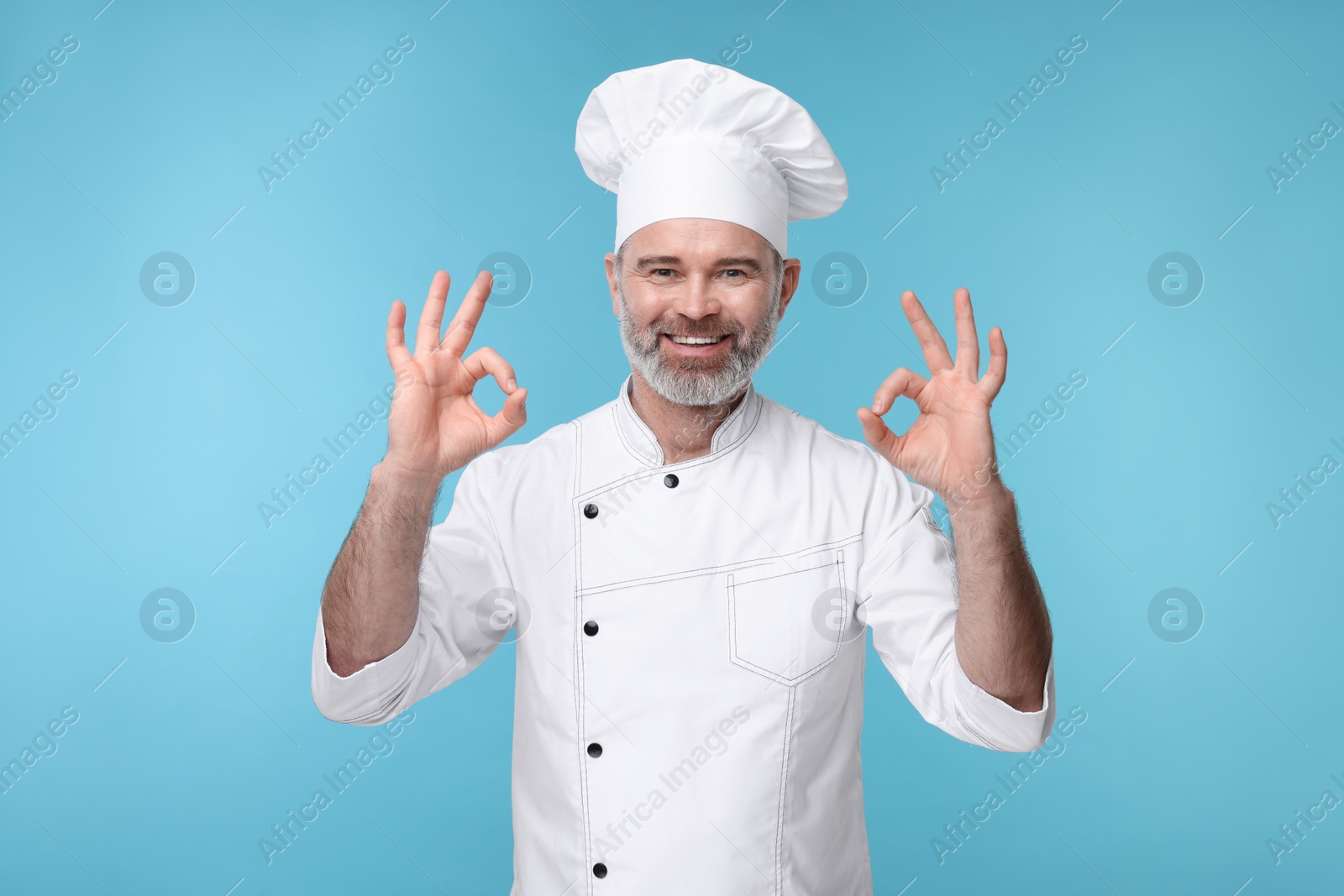 Photo of Happy chef in uniform showing OK gesture on light blue background