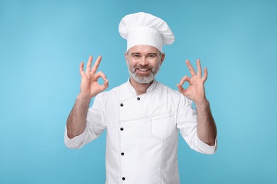 Happy chef in uniform showing OK gesture on light blue background