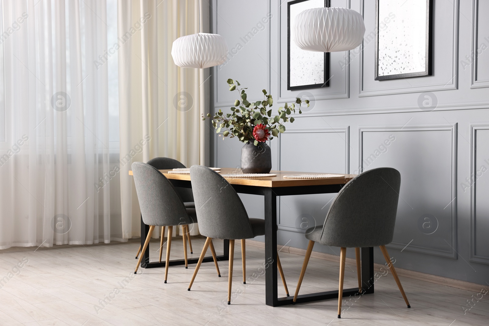 Photo of Soft chairs, table and vase with plants in stylish dining room