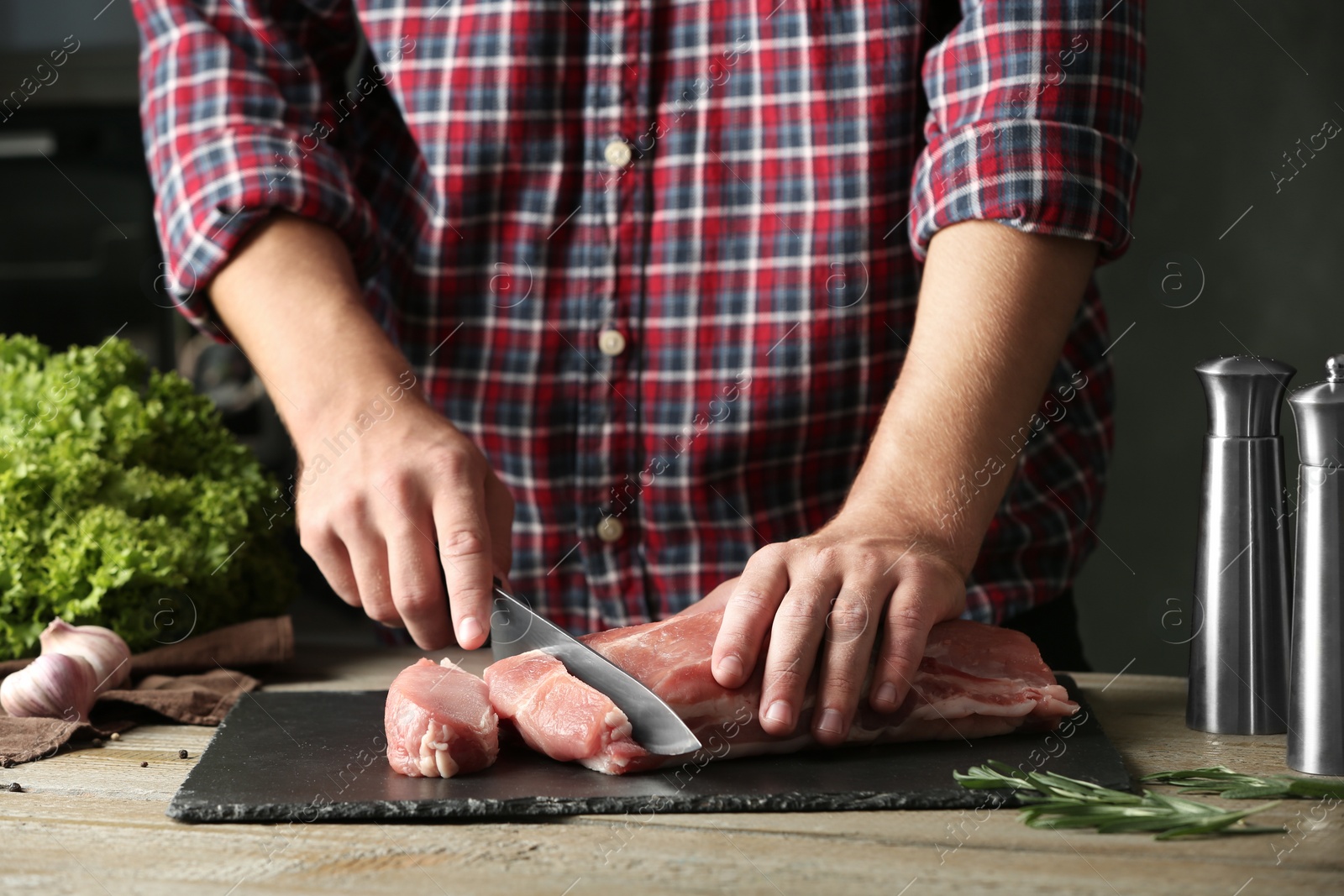 Photo of Man cutting fresh raw meat on wooden table, closeup