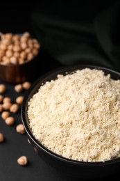 Photo of Chickpea flour in bowl and seeds on black table, closeup