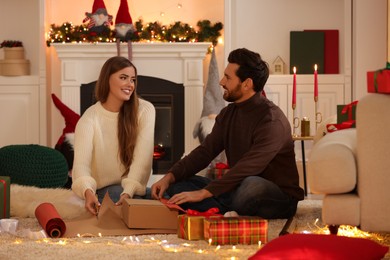 Photo of Happy couple decorating Christmas gift with wrapping paper at home