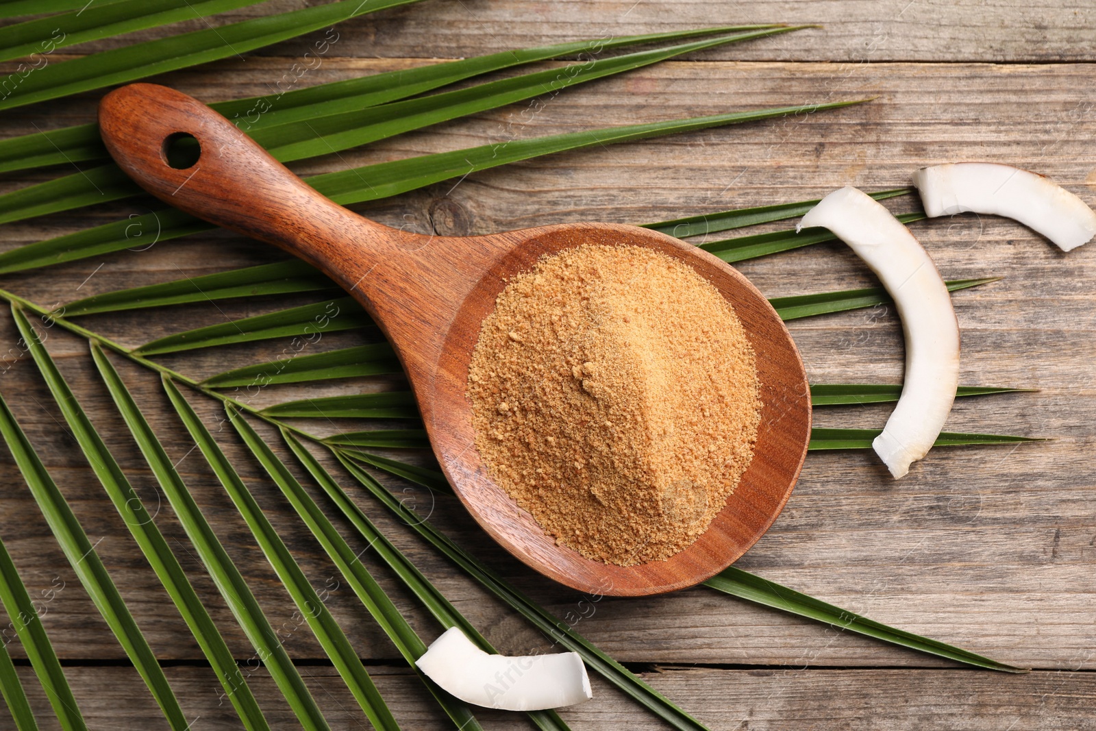 Photo of Spoon with coconut sugar, slices of fruit and palm leaves on wooden table, flat lay