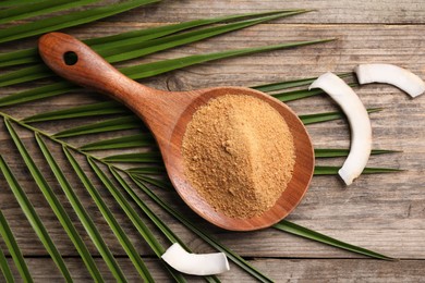 Photo of Spoon with coconut sugar, slices of fruit and palm leaves on wooden table, flat lay