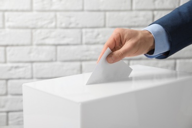 Photo of Man putting his vote into ballot box against brick wall, closeup