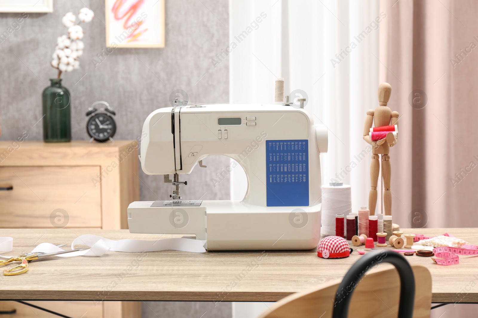 Photo of White sewing machine, cloth, craft accessories and mannequin on wooden table indoors