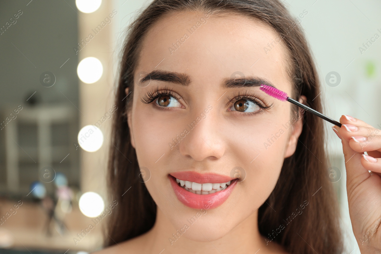 Photo of Attractive young woman applying mascara on her eyelashes against blurred background