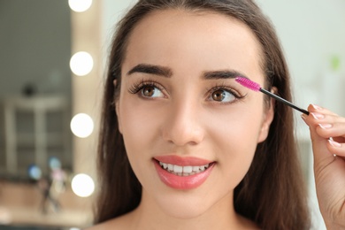 Attractive young woman applying mascara on her eyelashes against blurred background