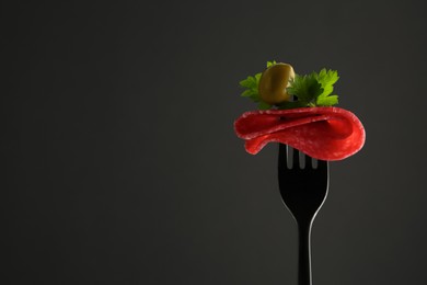 Fork with tasty slice of salami, olive and parsley on black background, space for text