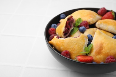 Photo of Bowl with delicious samosas, berries and mint leaves on white tiled table, closeup. Space for text