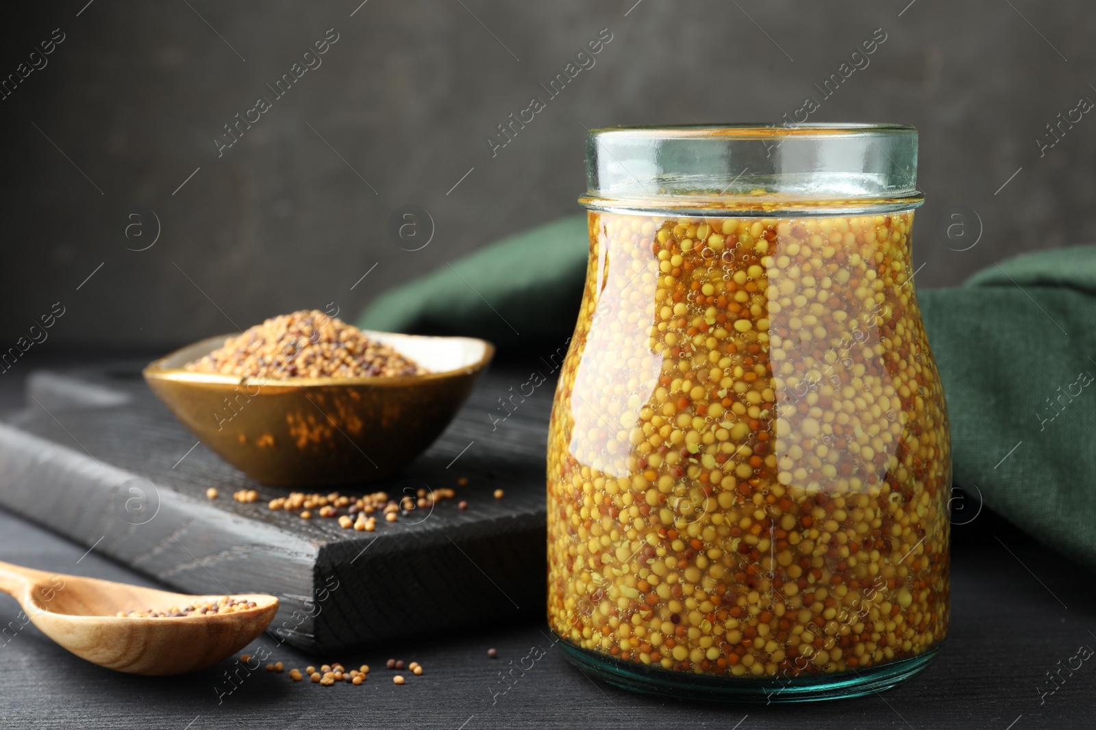 Photo of Whole grain mustard in jar and dry seeds on black wooden table