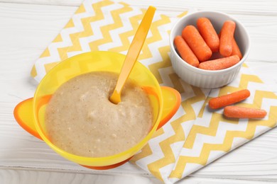 Photo of Baby food. Puree in bowl and small carrots on white wooden table