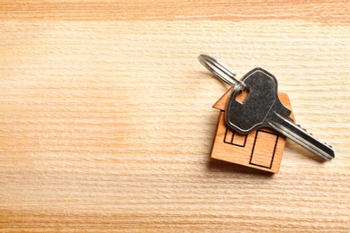 Key with trinket in shape of house on wooden background. Real estate agent services