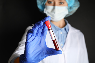 Photo of Scientist holding test tube with blood sample and label CORONA VIRUS against black background, focus on hand