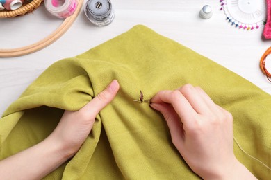 Photo of Woman with sewing needle and thread embroidering on cloth at white wooden table, top view