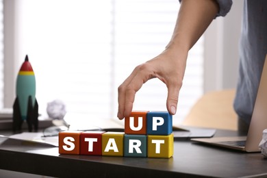 Woman forming words Start Up with colorful cubes at table in office, closeup. Space for text