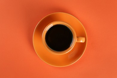 Photo of Coffee in cup on orange background, top view