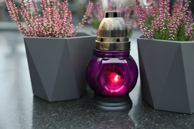 Photo of Grave light and potted heather on granite surface at cemetery, closeup